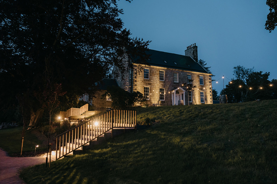 Evening shot of Elrick House, lit by festoon lights and stair lights.