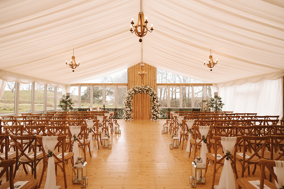 Wedding ceremony set up in the Garden Marquee at House of Elrick with golden chandeliers, chiavari chairs, silver lanterns and a flower arch.