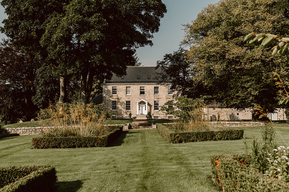 Exterior of country house wedding venue, House of Elrick, on Elrick Estate in Aberdeenshire. Blue skies in background and lush manicured gardens in foreground.