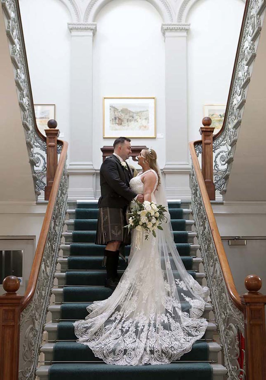 Bride and groom look into each others eyes standing on regal staircase