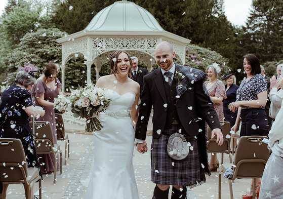 Bride and groom smile as they walk through confetti