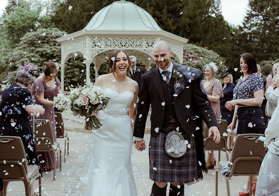 Bride and groom smile as they walk through confetti