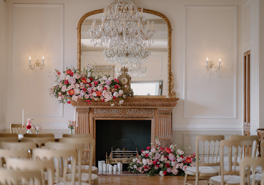 Ceremony room with large fireplace and chandelier, decorated with pink and red flowers