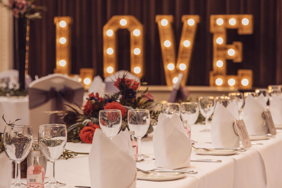 Love lights in background with view of long tables set up for wedding meal with red roses