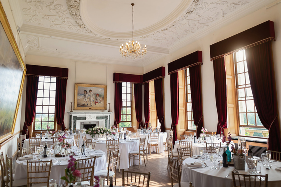 Wedding meal set up with round tables and chiavari chairs at Rowallan Castle, featuring baronial details around the room such as paintings and ceiling design.