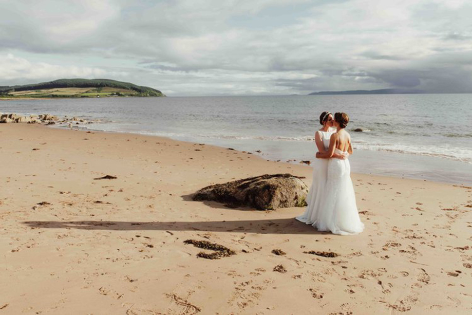 Two brides embrace in a kiss on a sandy beach