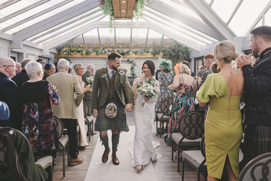 Bride and groom smiling as they walk back down the aisle with guests clapping