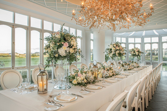 Floral decorated top table with large chandelier above and large bouquets of flowers