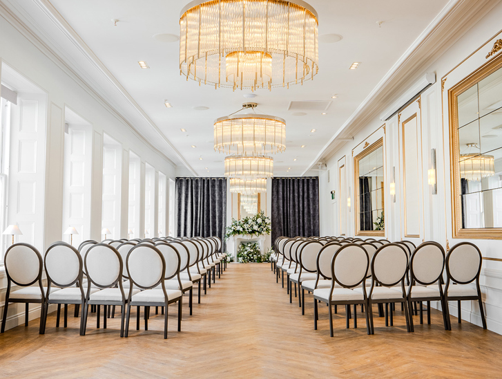 The Exchange wedding venue in Glasgow's ceremony room, with chandeliers, mirrors on walls and floral display at altar.