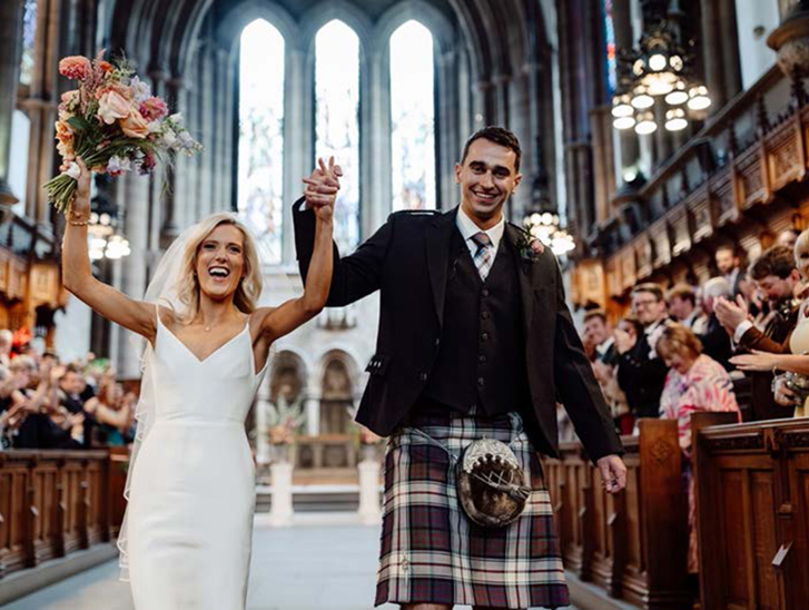 Bride and groom celebrate while walking back up the aisle hand-in-hand while guests clap in the Memorial Chapel at the University of Glasgow.